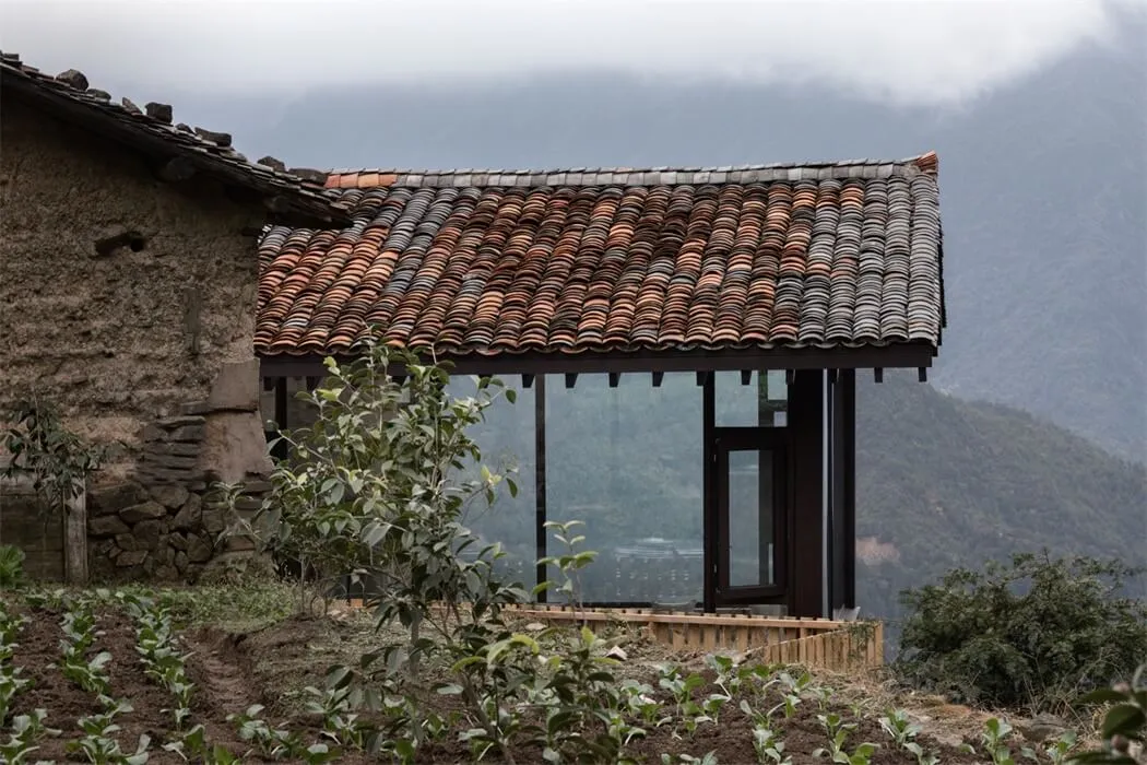 一座傳統住宅,擁有陶瓦屋頂與玻璃入口,背景為山景。