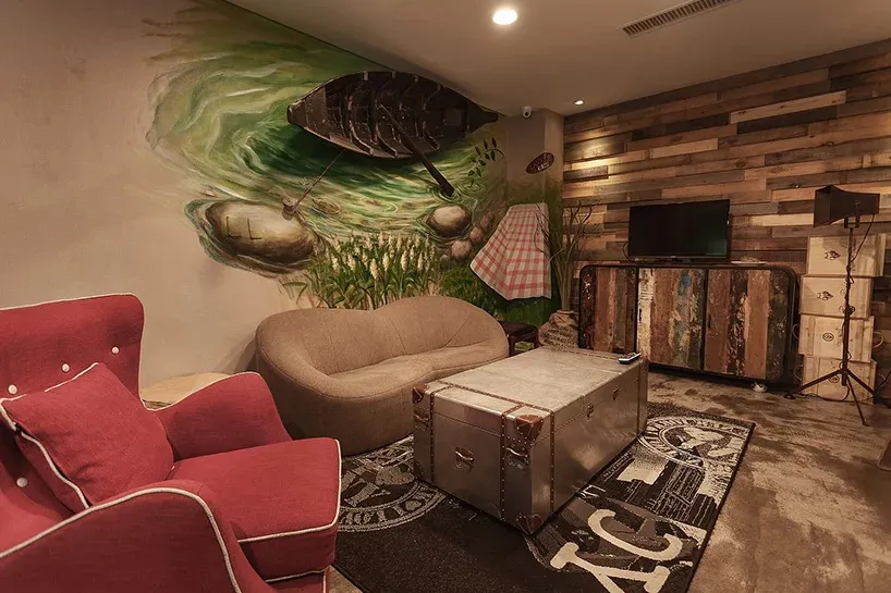 A cozy industrial-style living room with a retro trunk as a centerpiece, wooden panel walls, and a mural of a fishing boat on