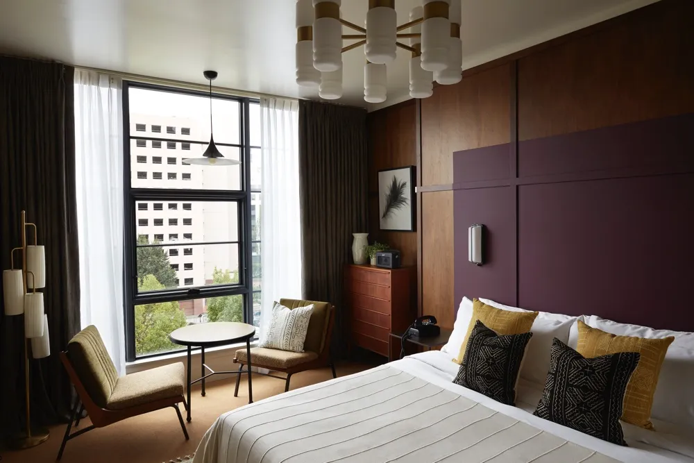 A modern hotel room featuring wooden paneling, fabric bedding, and metal accents.