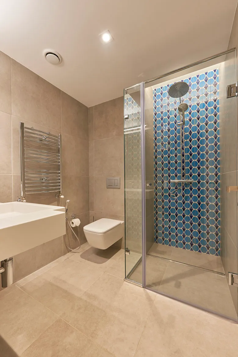 Modern minimalist bathroom with blue and white tile shower, white square sink, glass shower enclosure, and towel warmer.