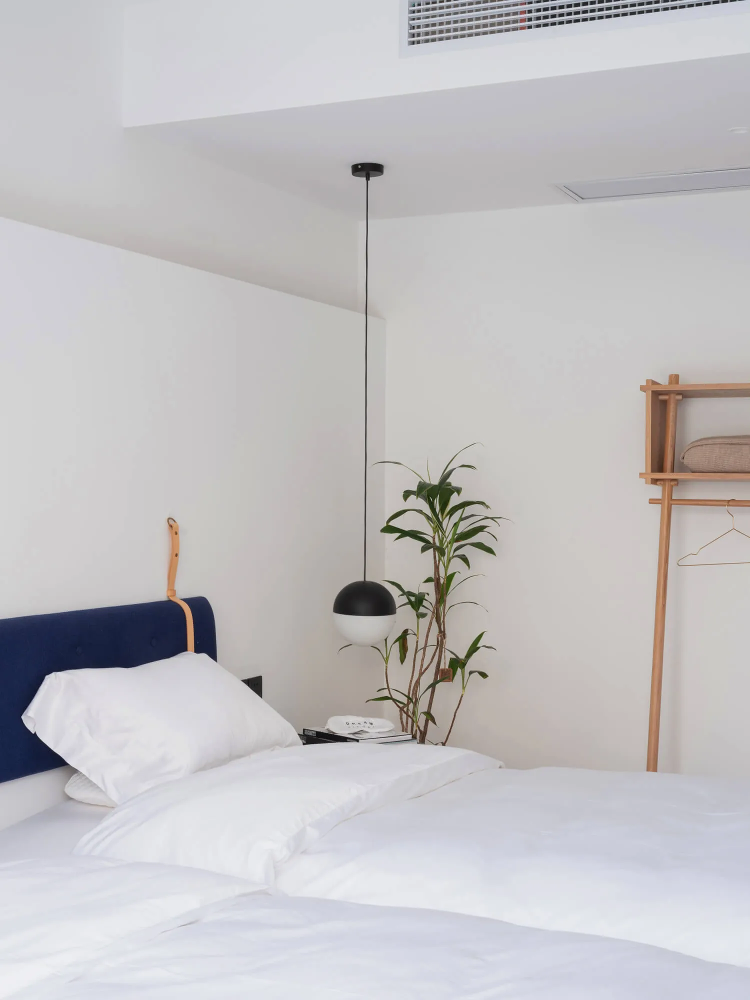 minimalist bedroom with a bed, textile headboard, wooden shelves, and a plant.