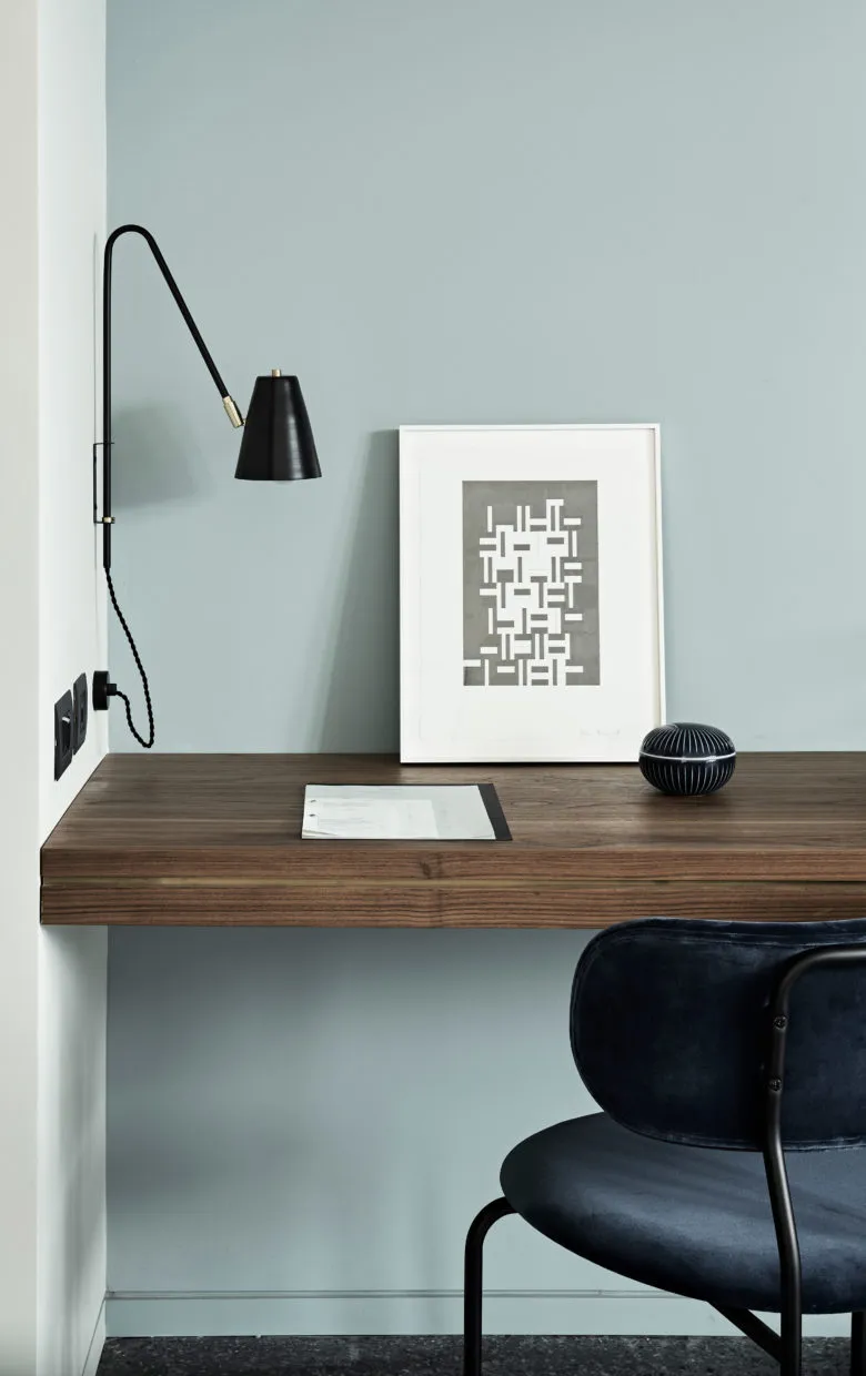 Minimalist office workspace featuring a wooden desk, a black swing arm lamp, and a framed abstract geometric print.
