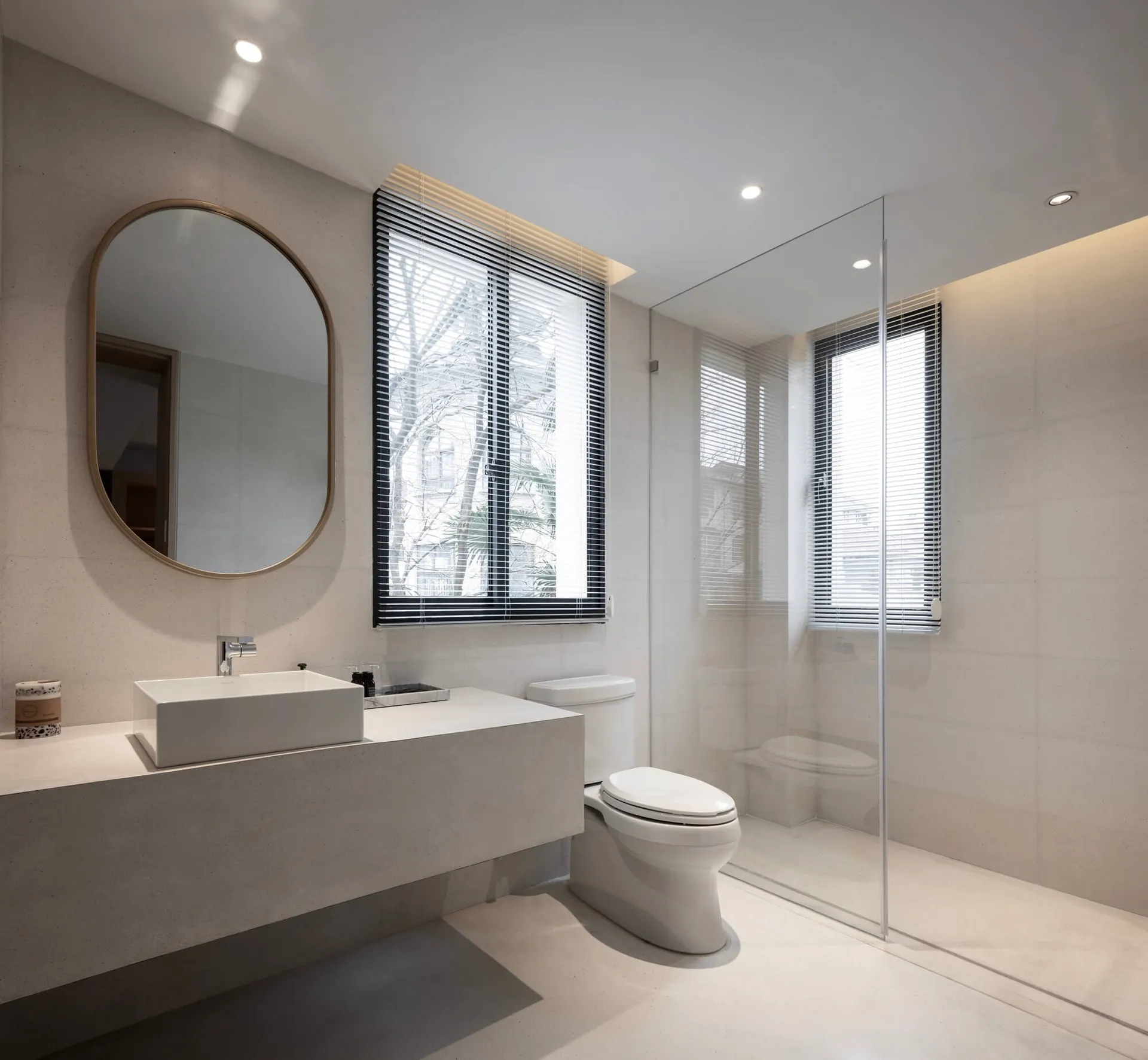 A modern bathroom with white concrete walls, a floating vanity, a large round mirror, and a clear glass shower enclosure.