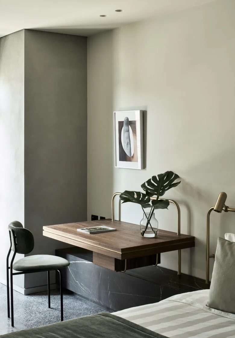 A modern living room featuring a wooden table with marble legs and a vase with monstera leaves.