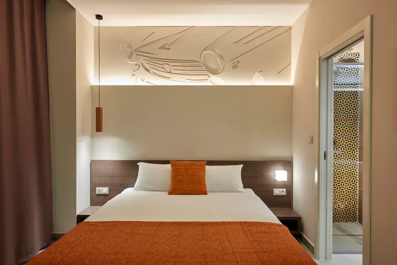 A modern minimalistic bedroom with a white bed and orange bedding and decorative wall features.