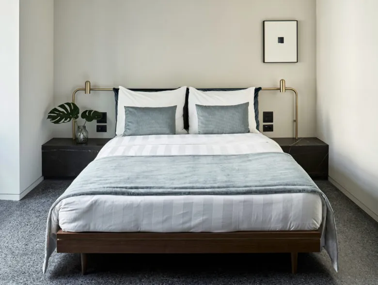 Modern minimalist bedroom featuring a wooden bed frame with metal handles, white bedding, and dark grey accents.