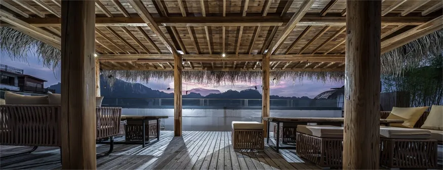 Vacation resort retreat terrace with wood-concrete-straw seating and scenic view of mountains and sunset.