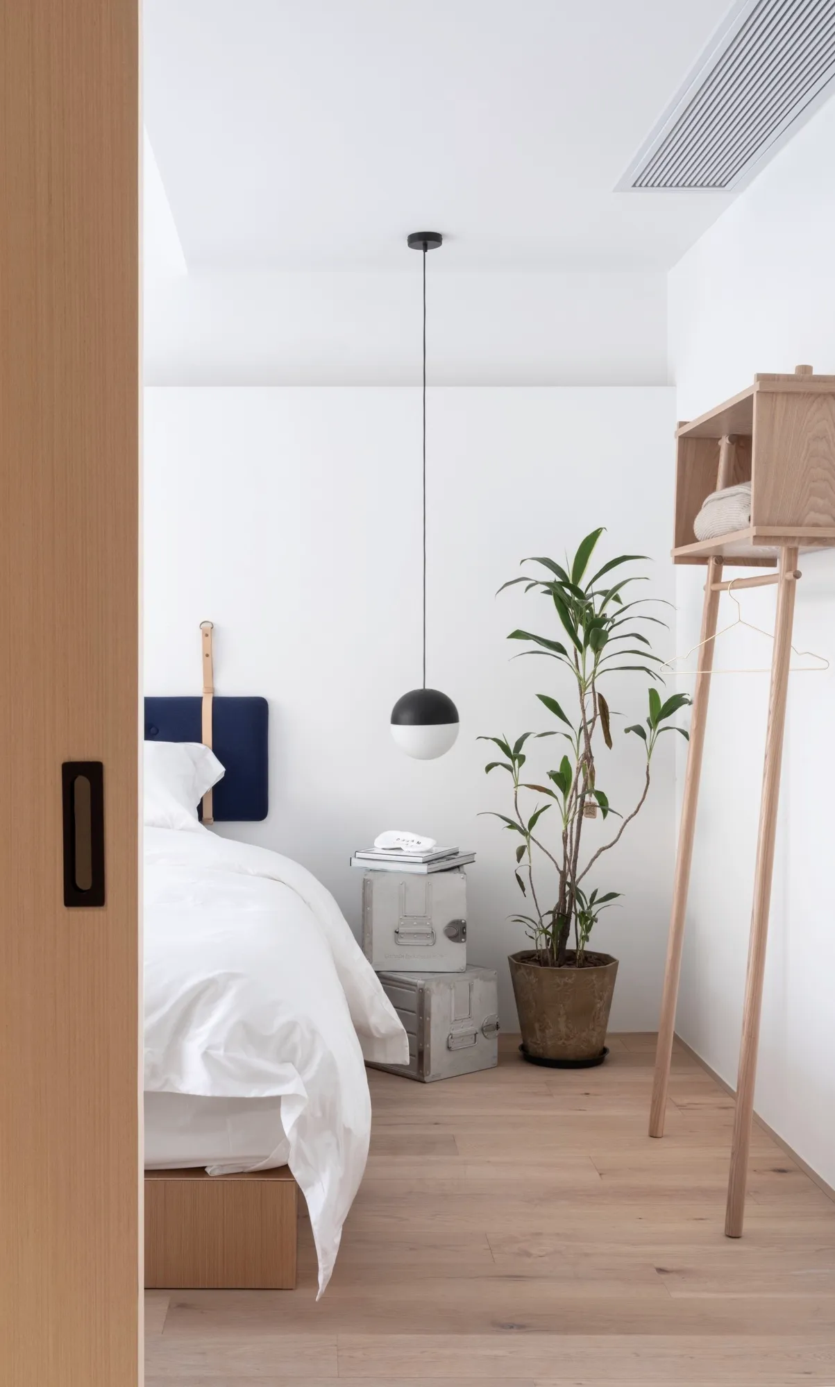 Minimalist bedroom with wooden furniture, metal accents, and potted plant.