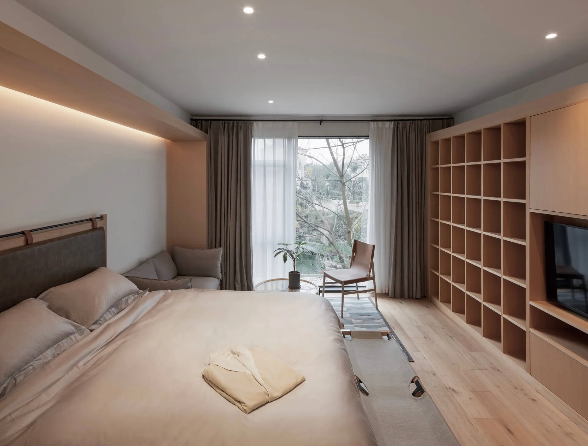 A minimalist bedroom featuring wood elements, a comfortable bed, and a large window.