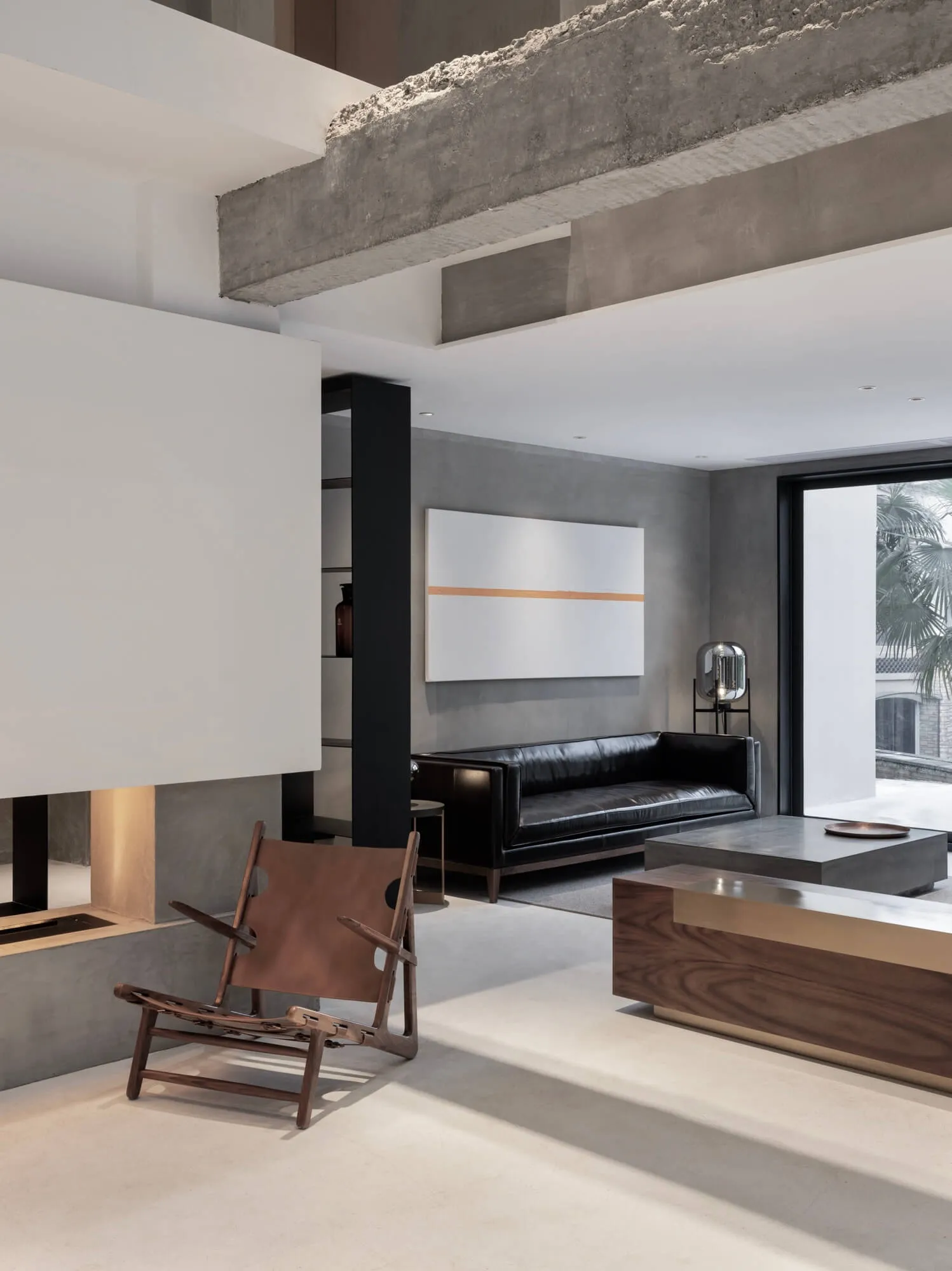 Modern minimalist living room with concrete walls, a black leather sofa, and wooden furniture.
