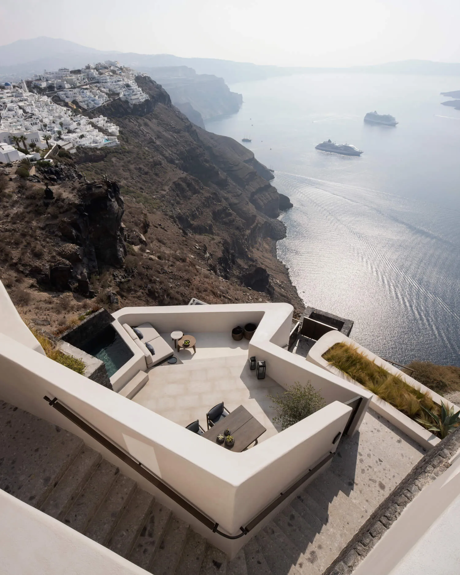 Modern cliffside vacation home with white stone and concrete design, featuring plants and a view of the ocean.