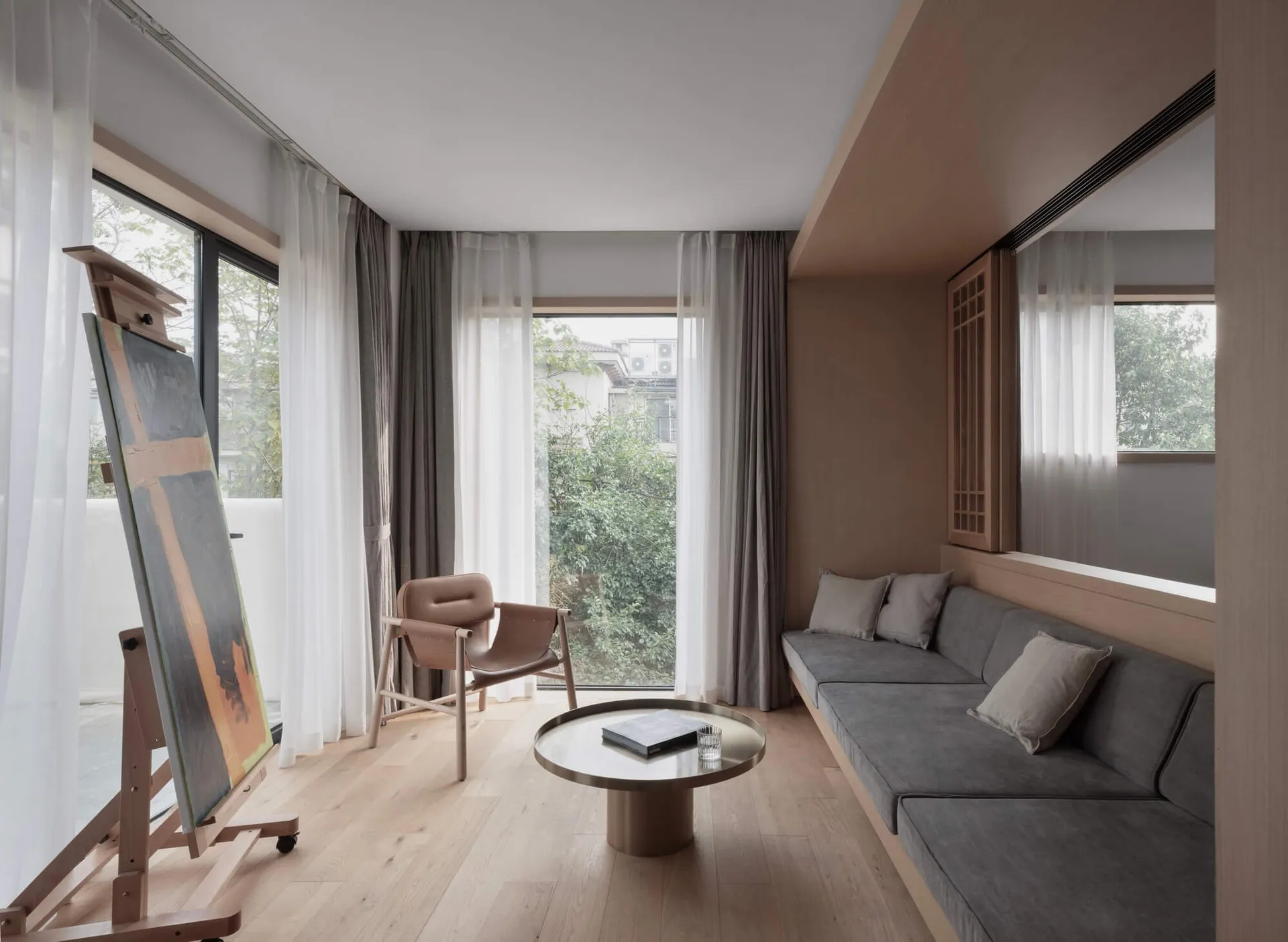 A modern living room with a wooden floor, a grey sofa, a round coffee table, and an easel with an abstract painting.