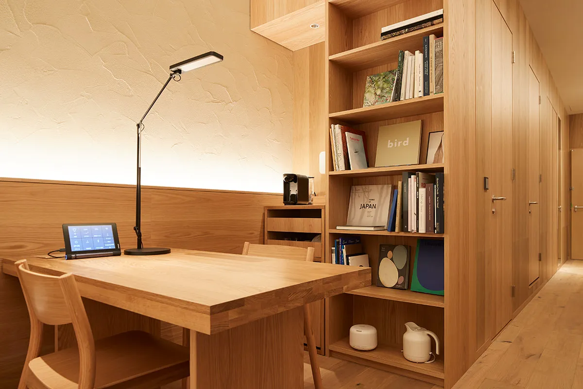 A minimalist workspace featuring a wooden desk and bookshelf filled with books and items.
