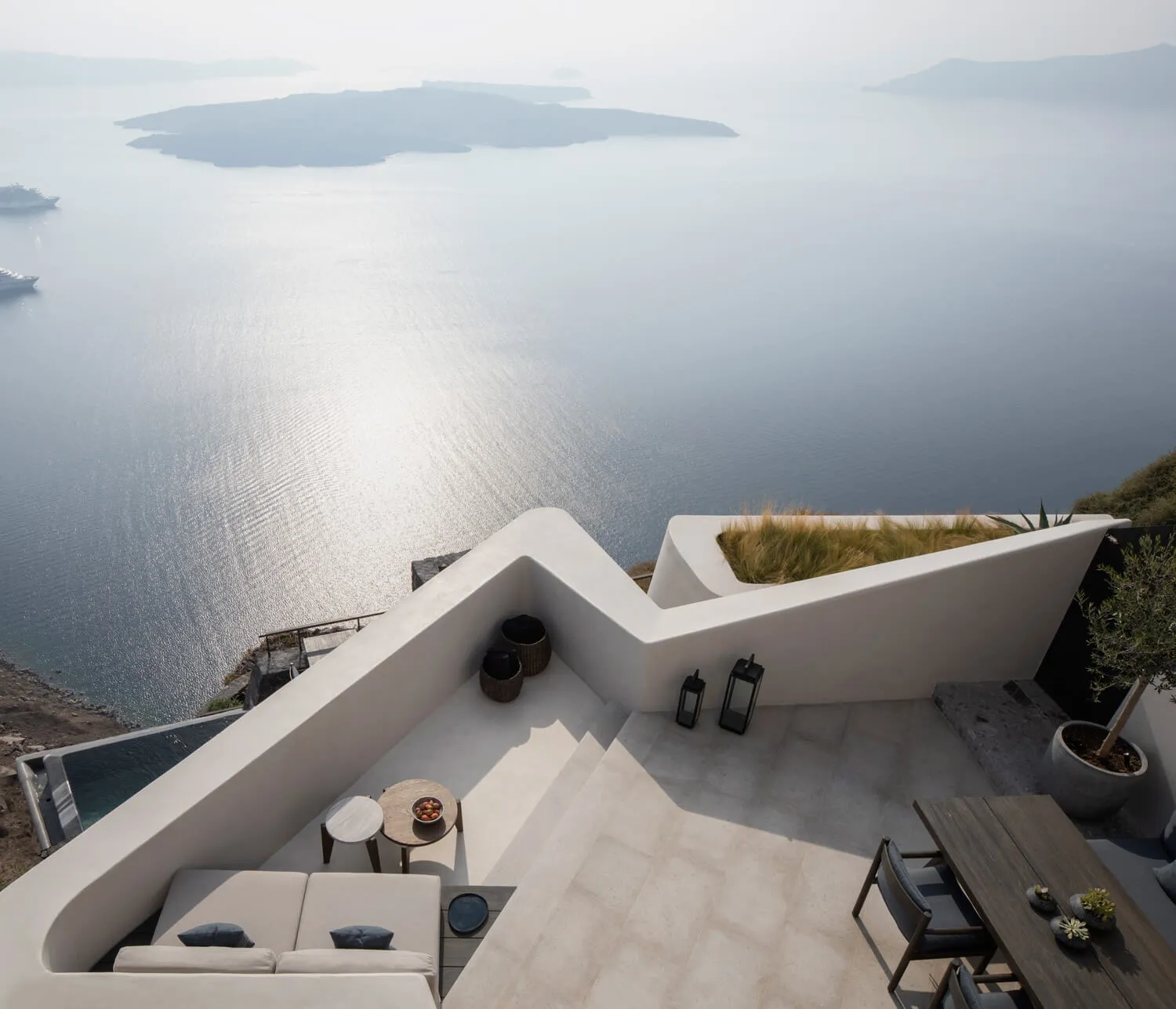 Modern minimalist terrace with concrete walls and seating area overlooking the ocean.