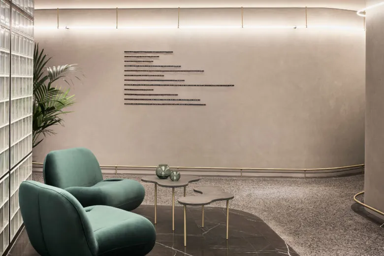 A modern lobby designed with concrete elements, featuring teal armchairs and abstract decorations.