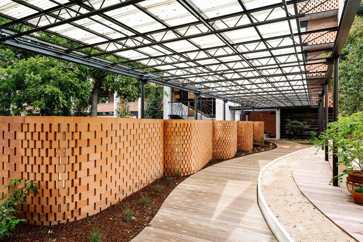 A modern garden with brick walls and wooden pathways under a glass ceiling.
