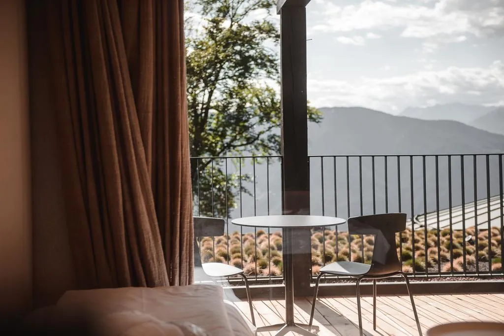 Minimalist residential balcony featuring two chairs, a table, and a view of mountains and foliage.