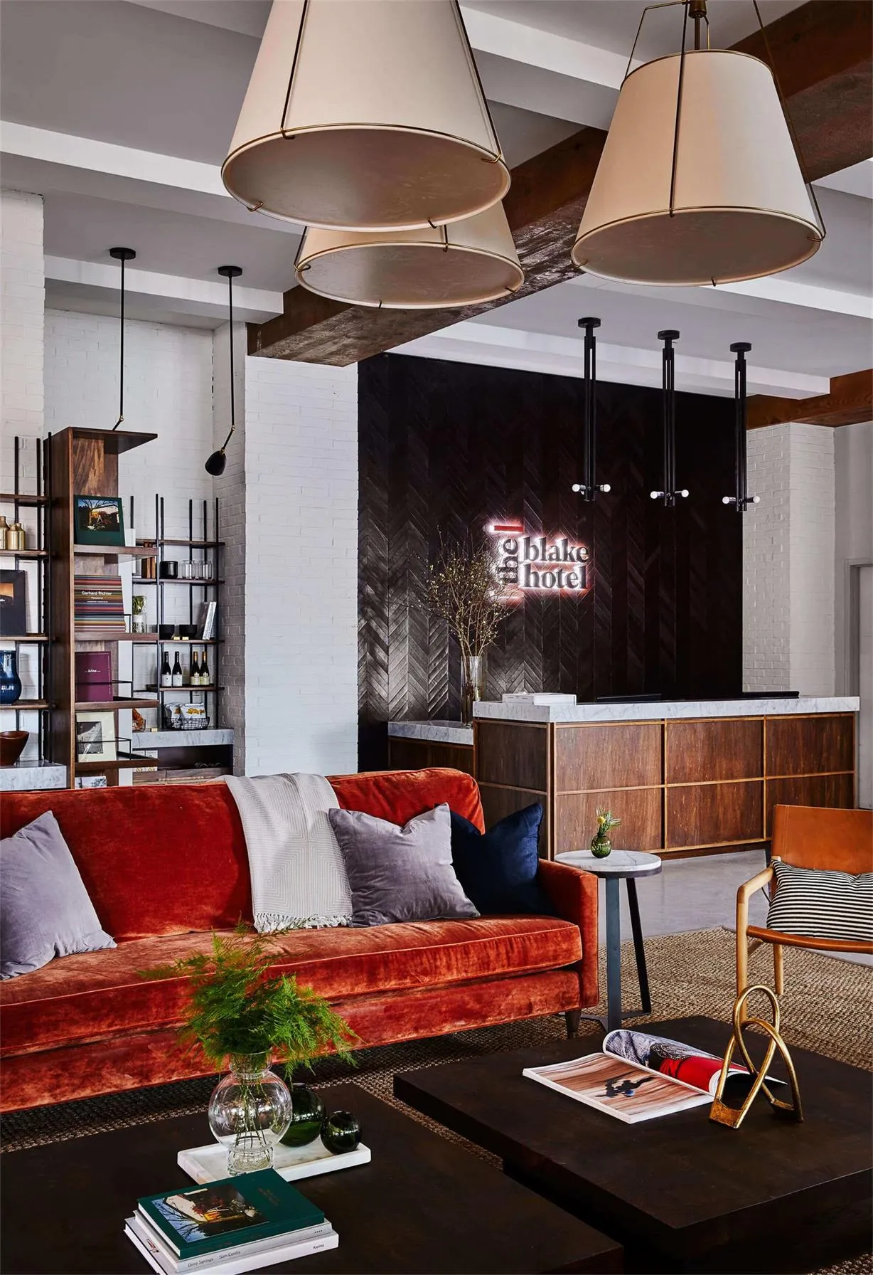 A modern industrial lobby featuring brick walls, a wooden reception desk, and a comfortable seating area with a red velvet so