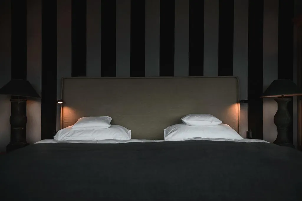 Modern minimalist bedroom with a double bed, white pillows, and a striped grey and black wall.