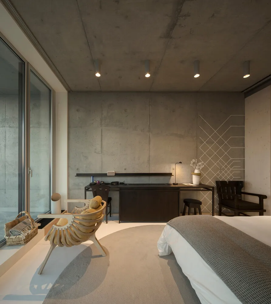 Modern minimalist bedroom with concrete walls, a large bed, and a sleek desk.