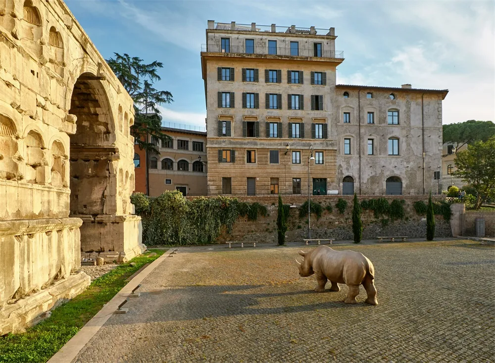 A rhinoceros statue stands on a stone pavement amidst ancient ruins and old buildings.