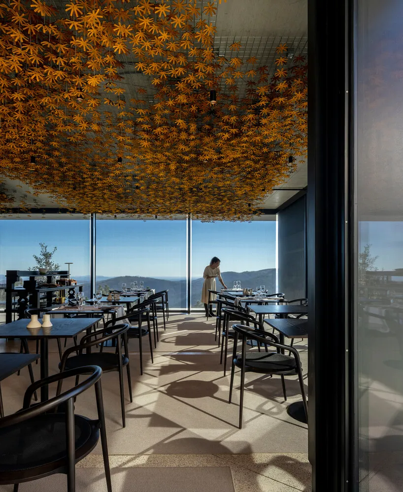 A modern restaurant interior featuring a concrete ceiling adorned with small, golden leaf-shaped elements.
