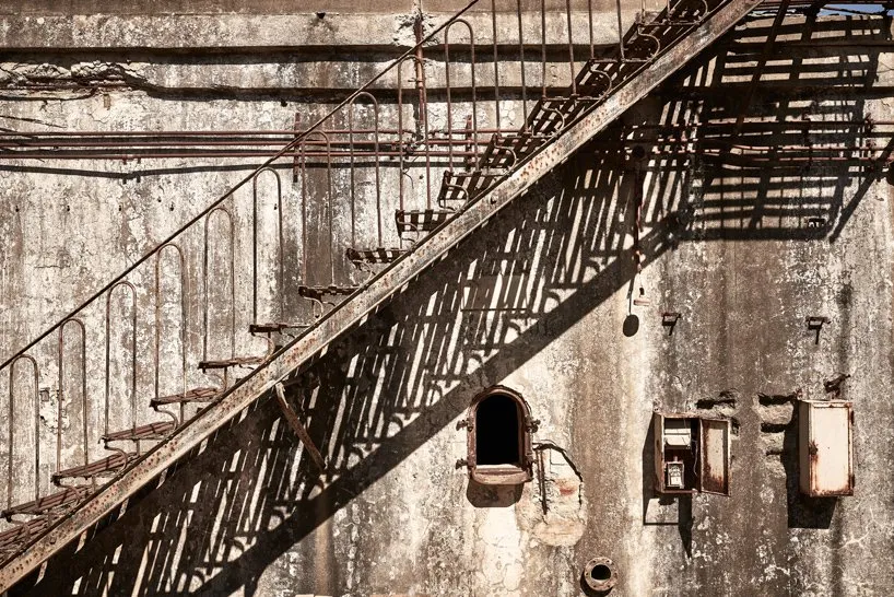 Rusted metal staircase on an abandoned industrial exterior with concrete walls.