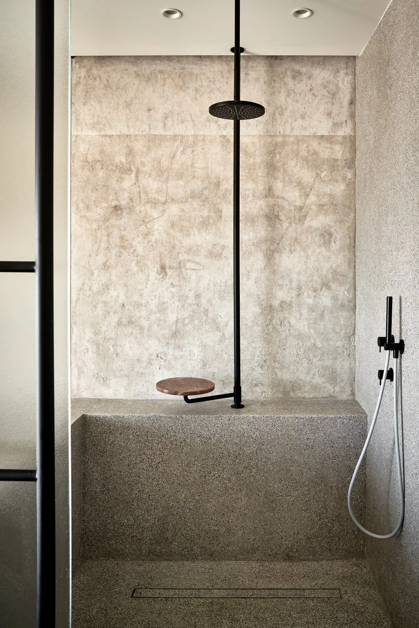 Minimalist bathroom with a stone shower featuring a concrete seat and a modern showerhead mounted on the wall.