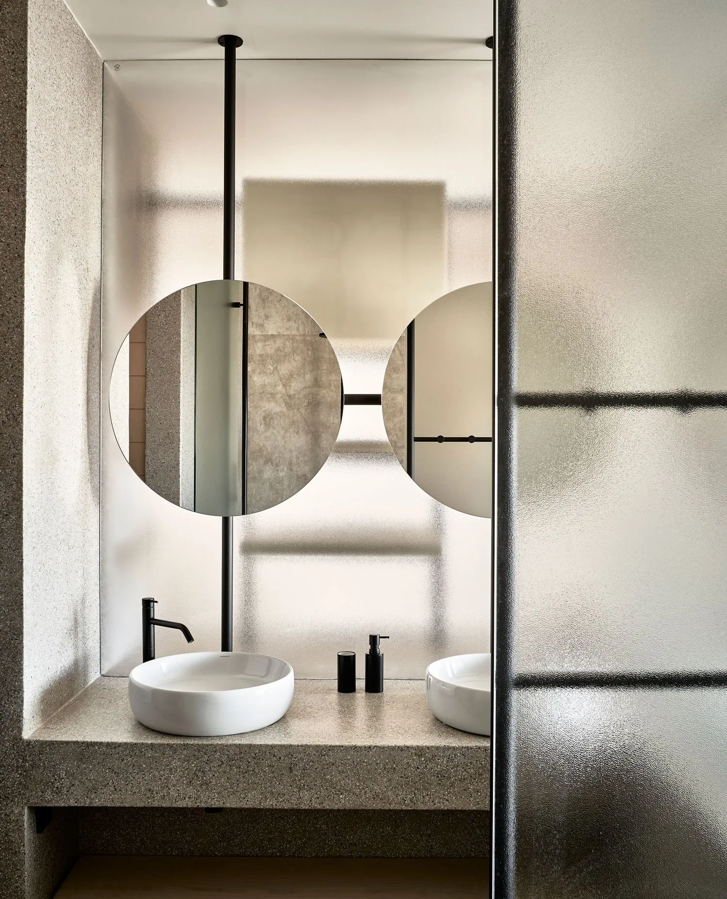 Minimalist bathroom with concrete finishes, modern sink, and circular mirrors