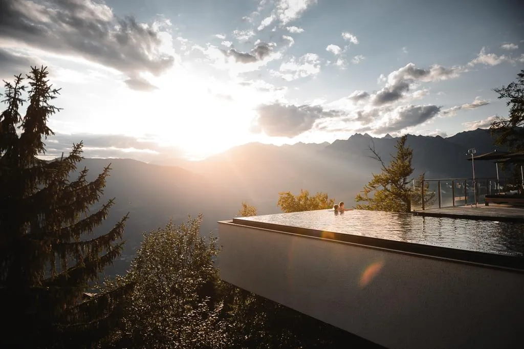 Two people enjoying an infinity pool with a stunning view of mountains during sunset.