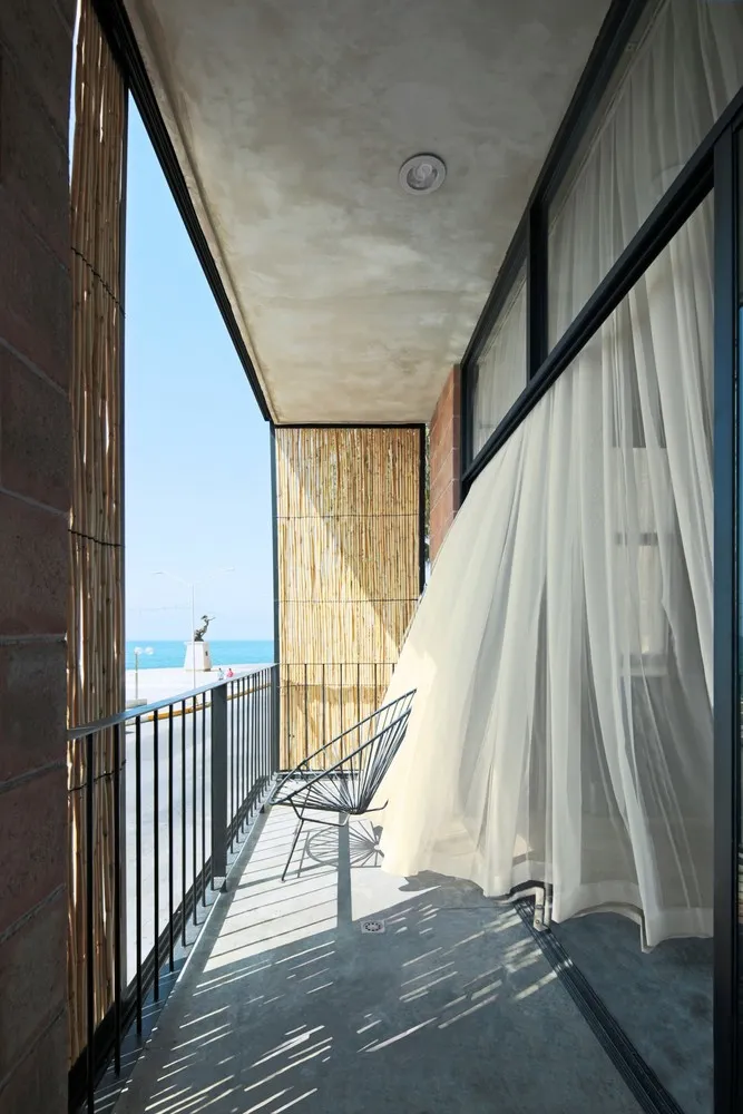 Modern balcony featuring a white curtain hanging from a ceiling fan, overlooking a beach.