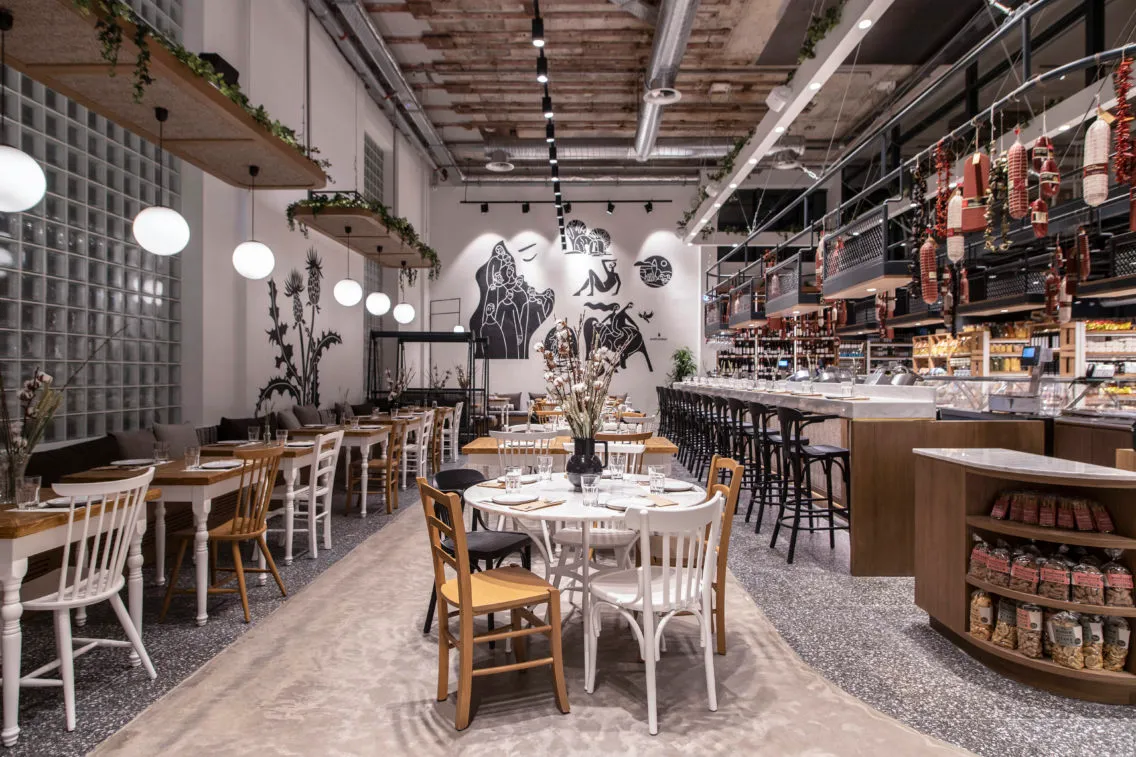 A modern cafe dining room with wooden tables, concrete flooring, and glass walls and shelves.