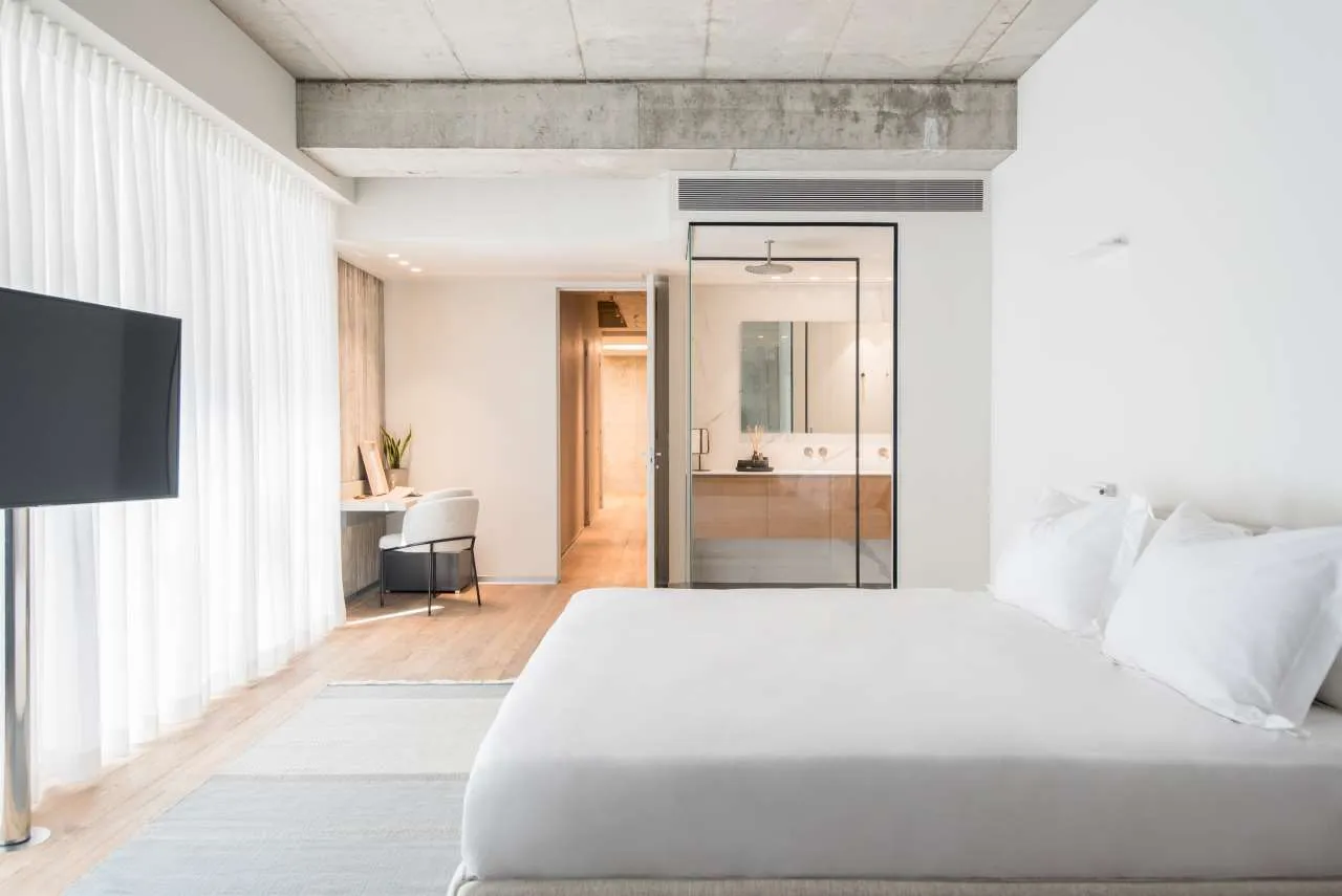 A minimalist bedroom with a white bed, white curtains, and a white desk in the background.