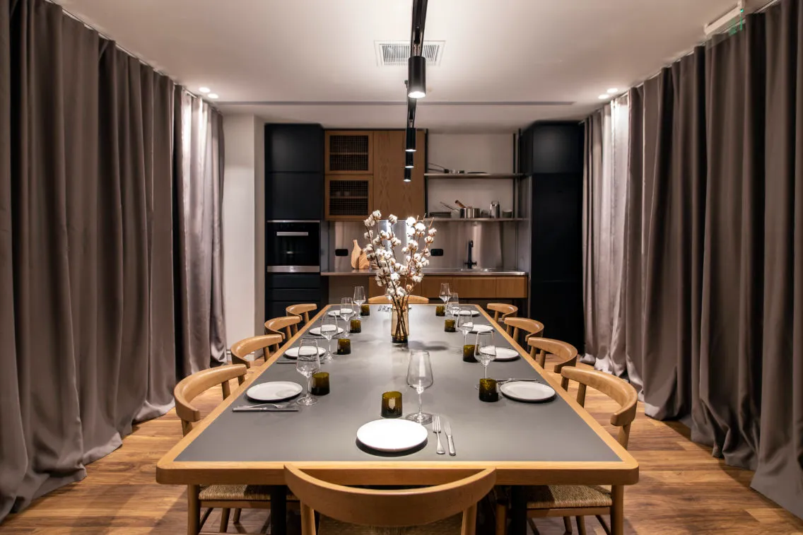 Modern dining room with wooden chairs, glass vase centerpiece, and gray table setting.