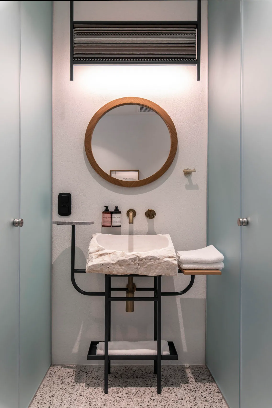 A minimalist bathroom featuring a concrete sink and mirror with a round wooden frame, and a towel rack mounted on the wall.