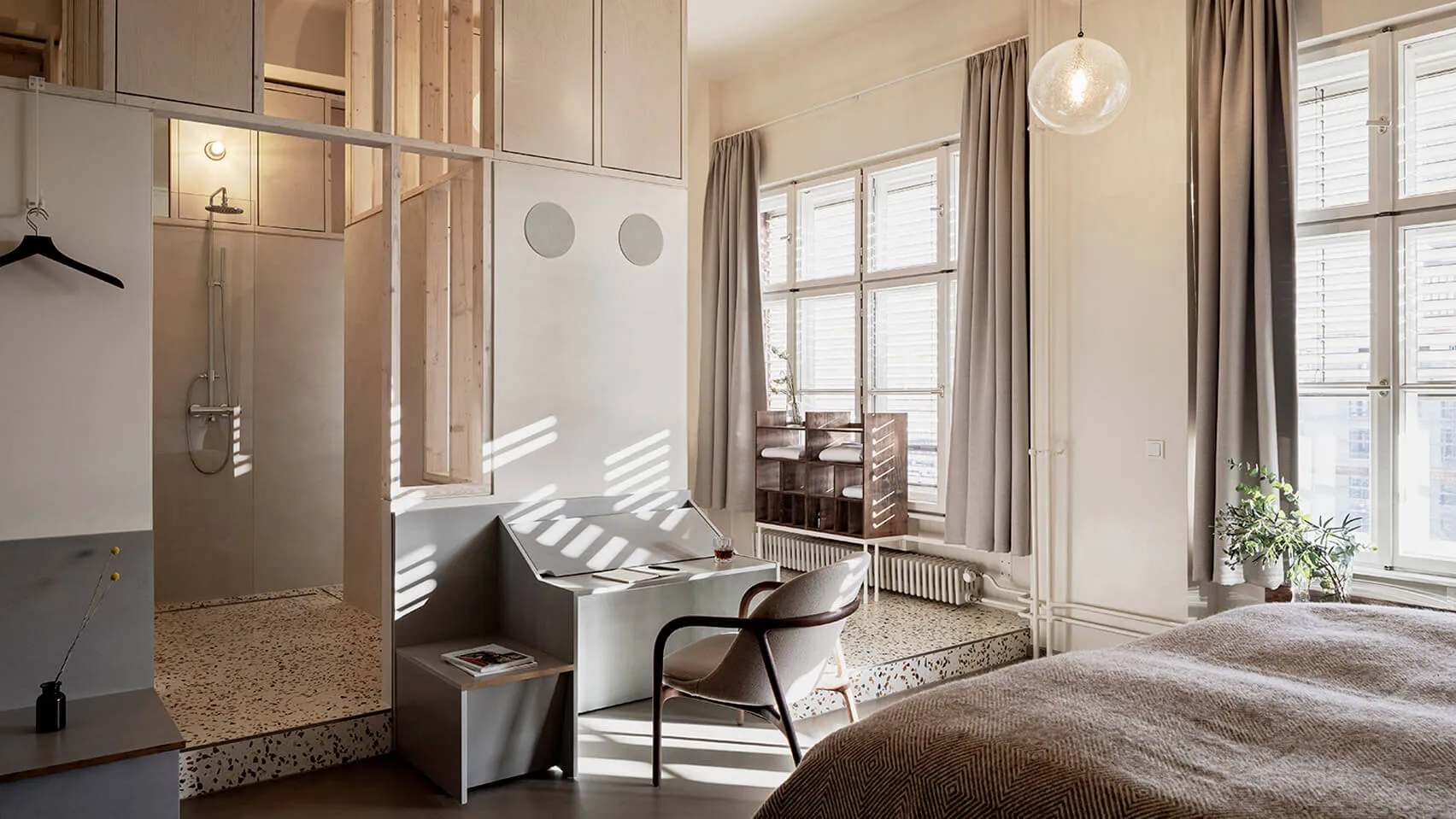 A minimalist bathroom featuring a white and marble floor with a walk-in shower and a sunlit room with a desk and chair.
