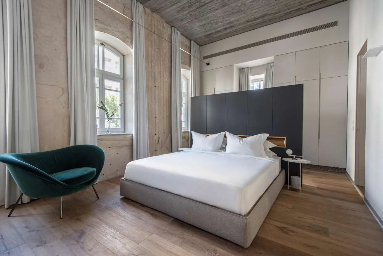 Modern minimalist bedroom with concrete walls, wood flooring, and a large window.