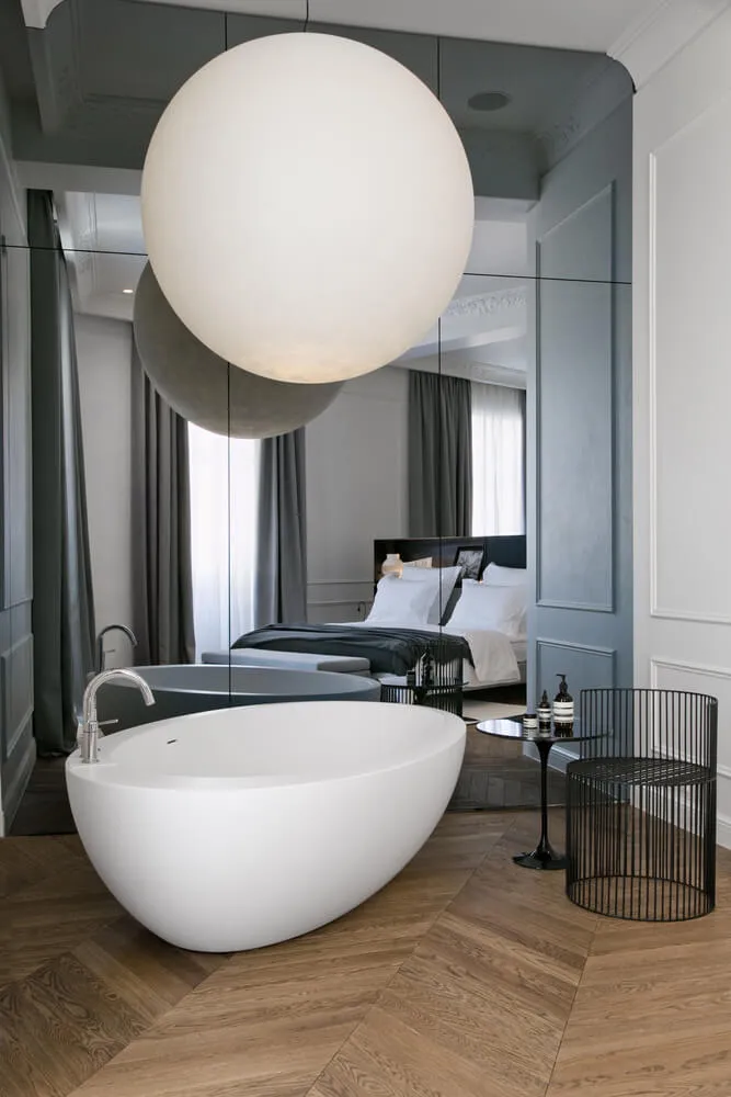 Modern bathroom with ceramic bathtub and metal accents, featuring a spherical light fixture and large mirrors.