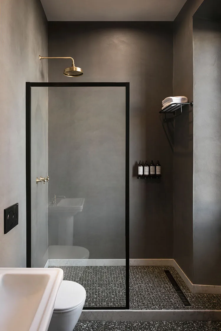 Modern bathroom with grey concrete walls, metal fixtures, and glass shower enclosure.