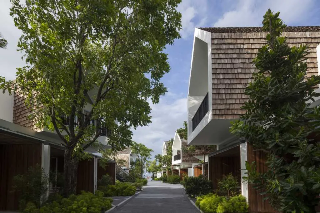 A modern residential exterior with wooden structures, glass doors, and concrete walkways.