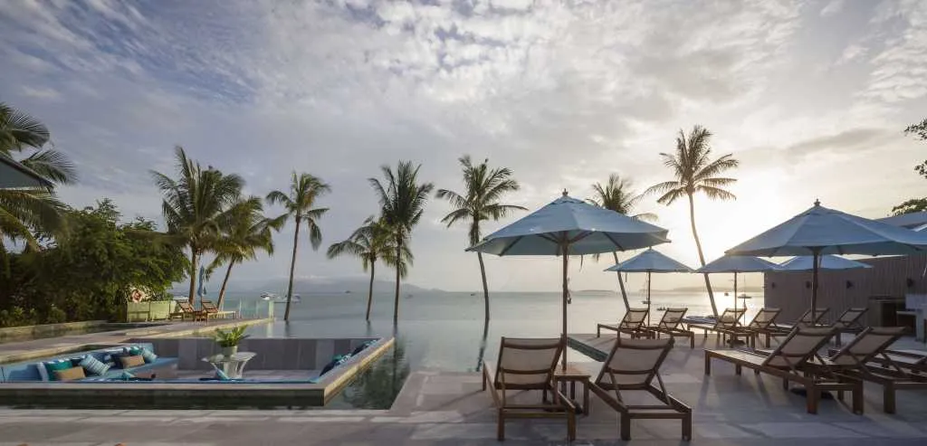 Poolside lounge area with umbrellas, deck chairs, and palm trees overlooking the ocean.