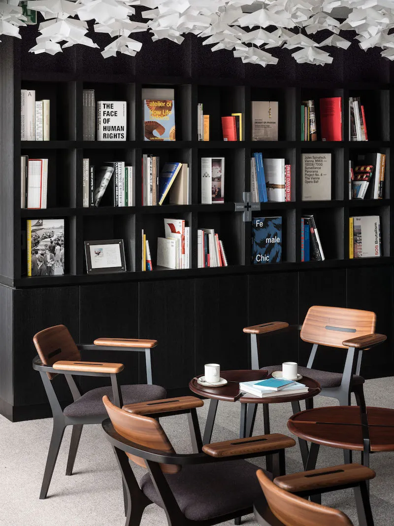 A modern library space with wooden chairs and a large bookshelf filled with books.