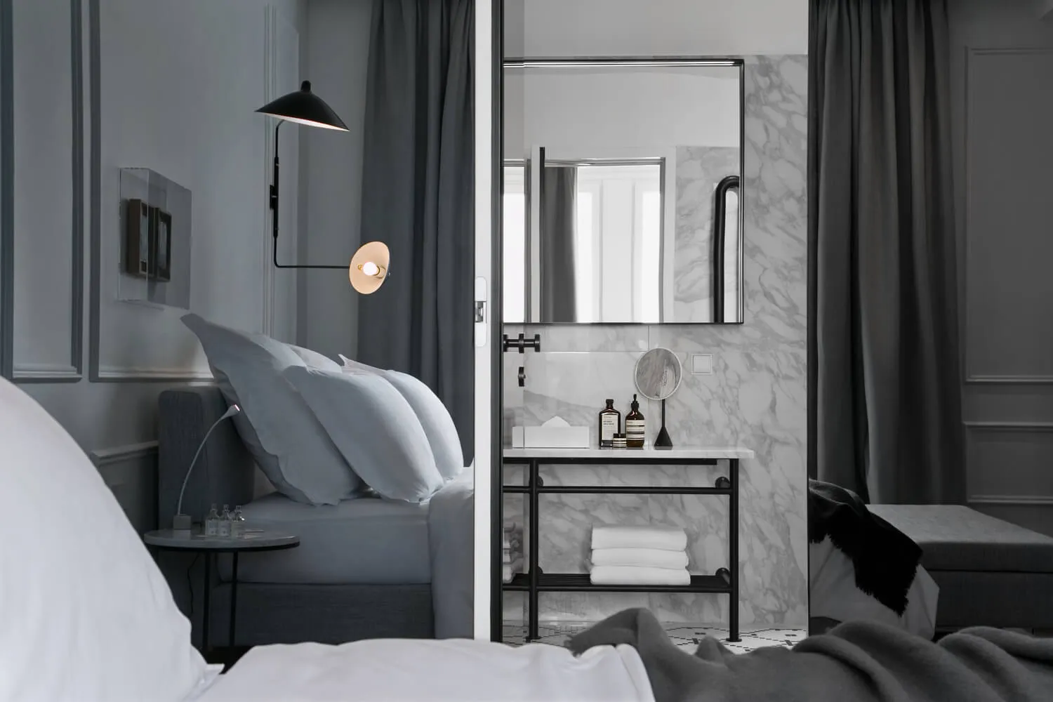 Modern minimalist bedroom with dark gray curtains, marble bathroom, and metal accents.