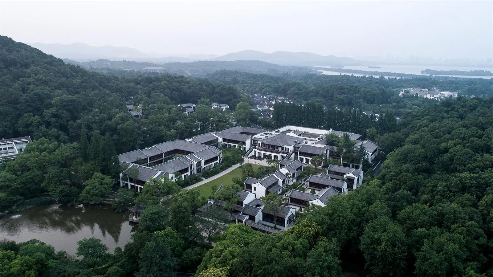 Aerial view of traditional residential buildings surrounded by lush greenery and a serene lake.