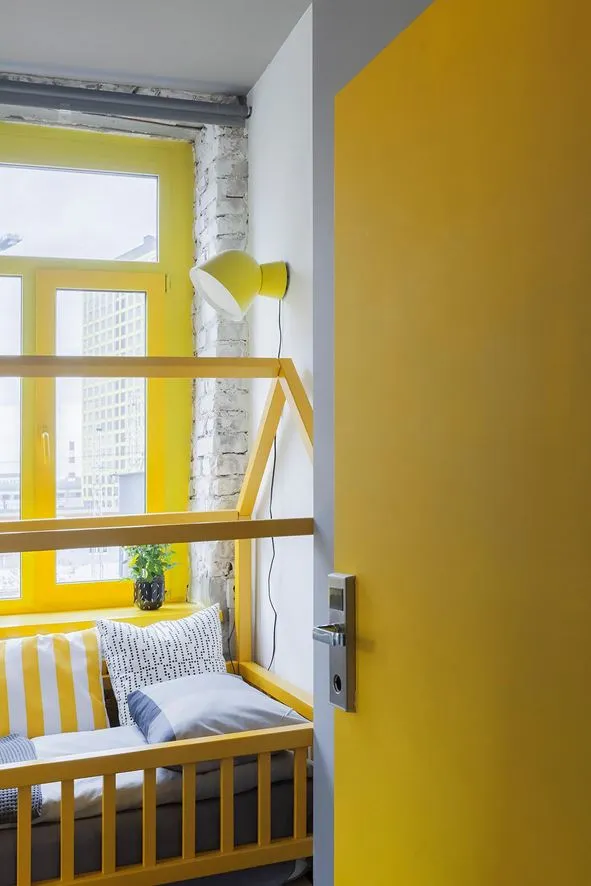 A minimalist bedroom with white walls, yellow accents, and a window with a city view.