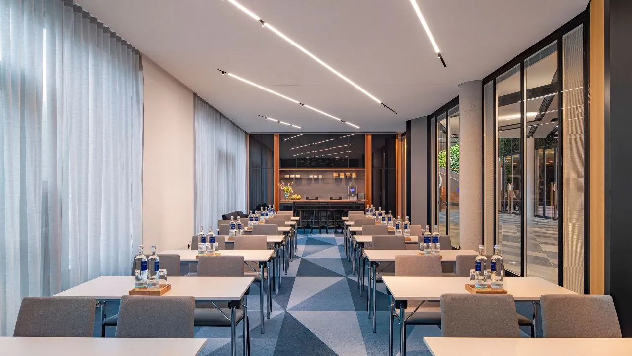 Conference room with modern design featuring concrete walls, glass partition, metal tables, and fabric-covered chairs.