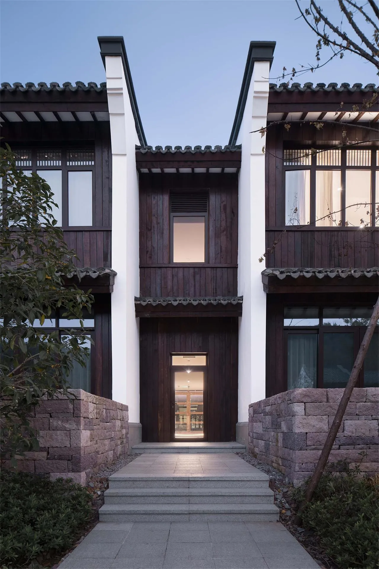 A modern exterior of a house composed of wooden and stone materials with large windows and a tiled roof.