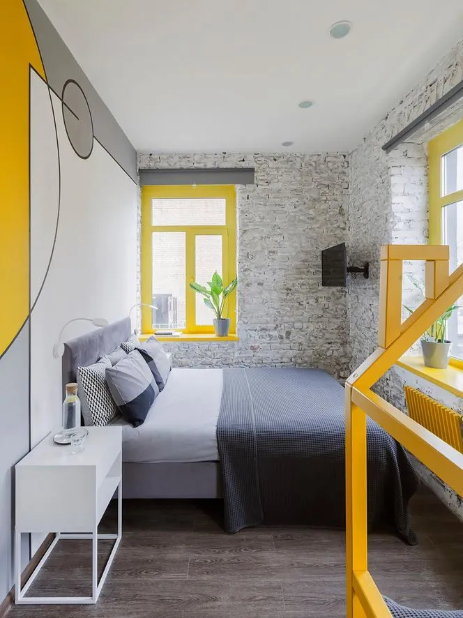 A modern bedroom featuring a concrete wall and wooden floor with a yellow window frame and a gray bed.