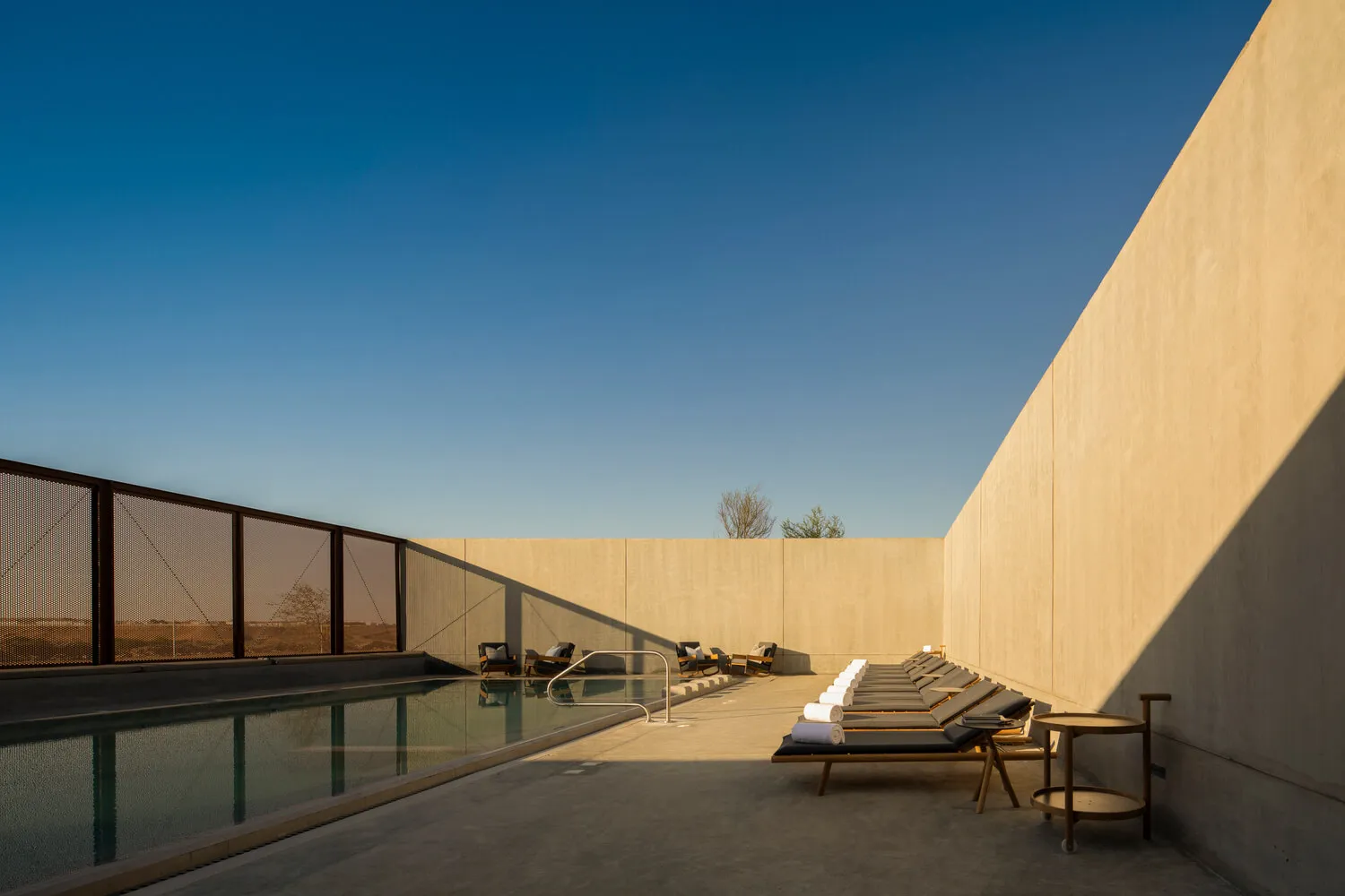 A modern swimming pool area with concrete walls and a clear blue sky.