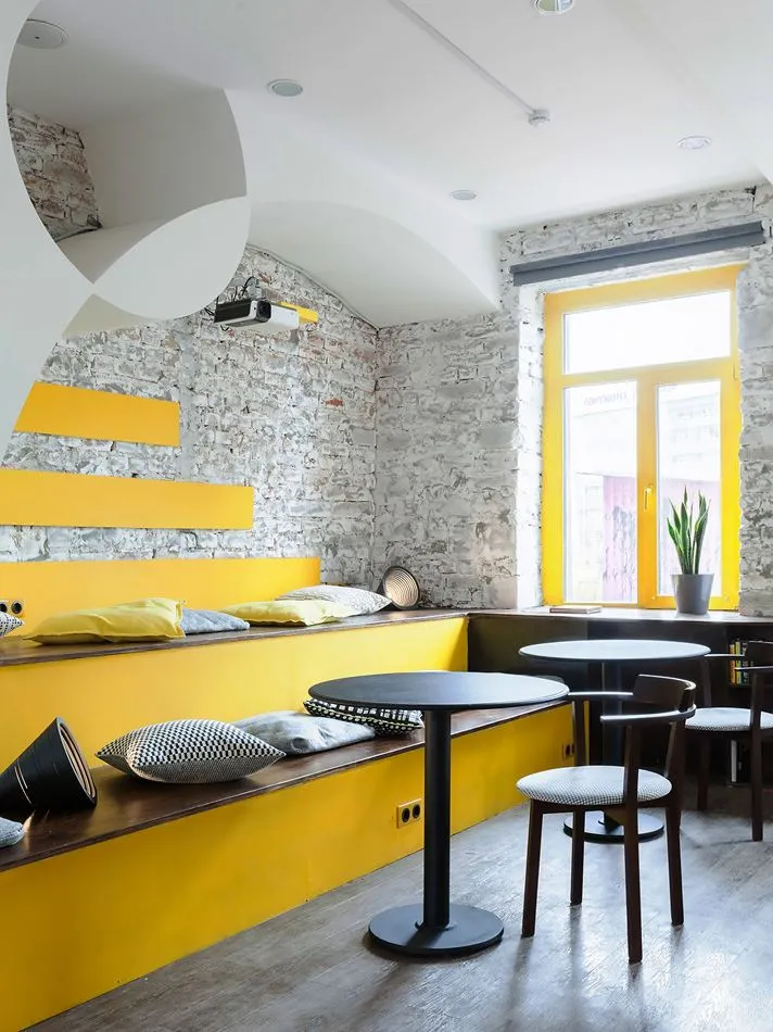 Modern cafe interior with yellow accents, seating, and tables.